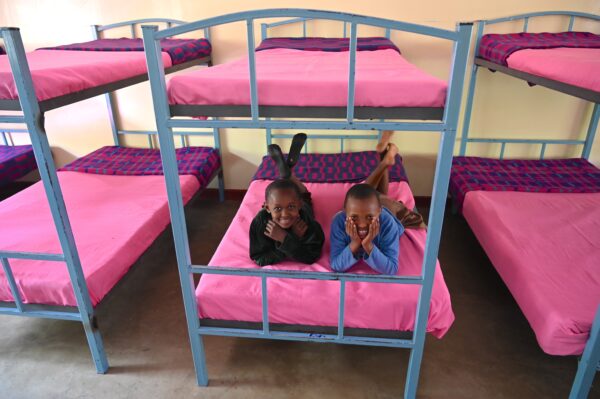 Two smiling children lying on a pink bunk bed in an MCF dormitory