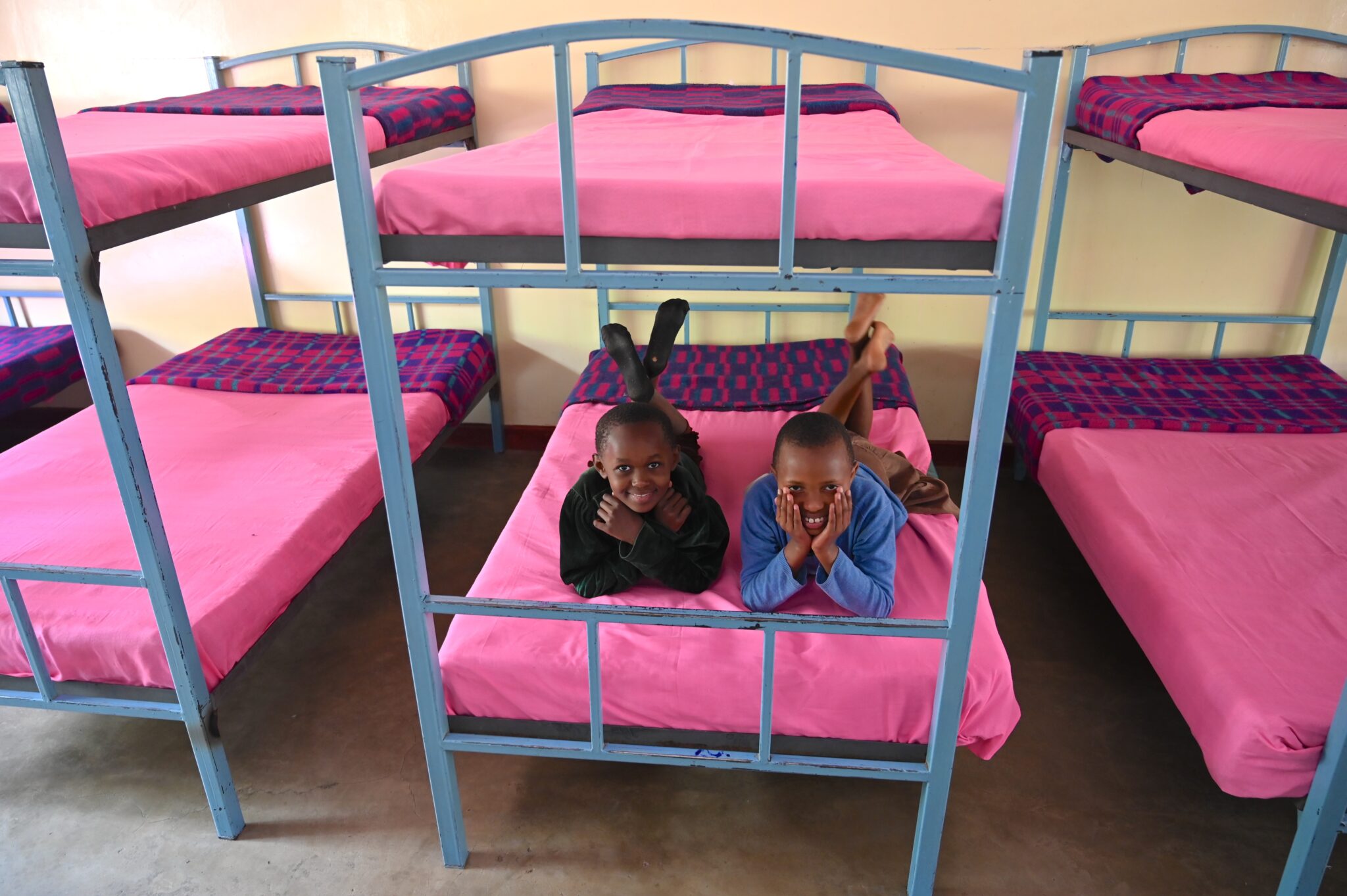 Two smiling children lying on a pink bunk bed in an MCF dormitory