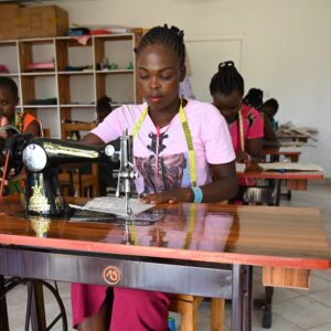 A young woman sewing at a treadle sewing machine in a vocational training classroom