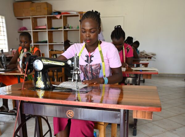 A young woman sewing at a treadle sewing machine in a vocational training classroom