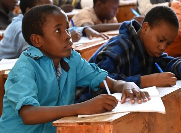 Two students writing at wooden desks in an MCF classroom