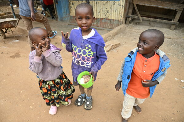 Three young children smiling, one holding a green bowl of food