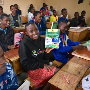 Smiling students in a classroom holding up their new textbooks