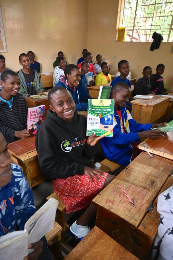 Smiling students in a classroom holding up their new textbooks