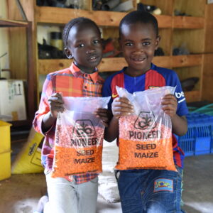 Two smiling children holding bags of maize seed