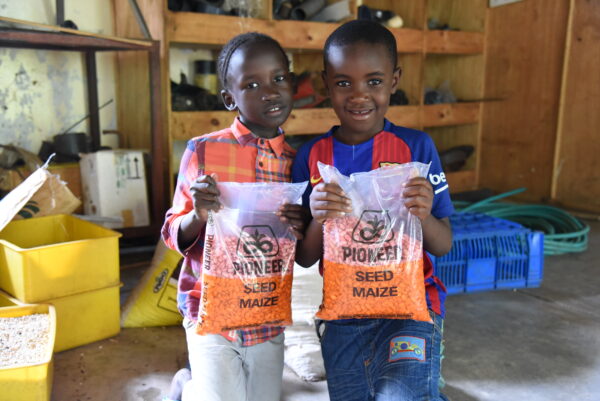 Two smiling children holding bags of maize seed