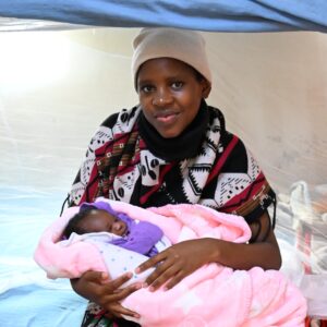 A young mother holding her newborn wrapped in a pink blanket beside a mosquito net