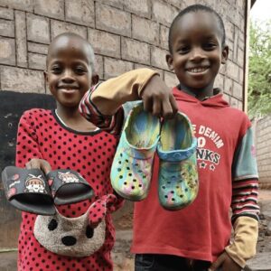 Two smiling children holding up pairs of Crocs