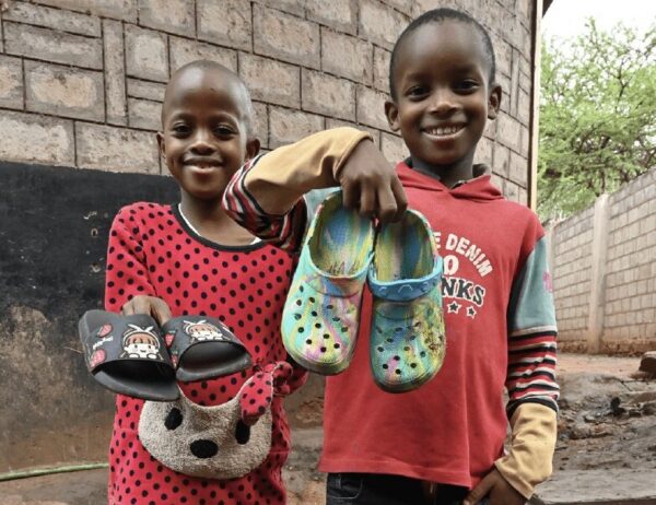 Two smiling children holding up pairs of Crocs