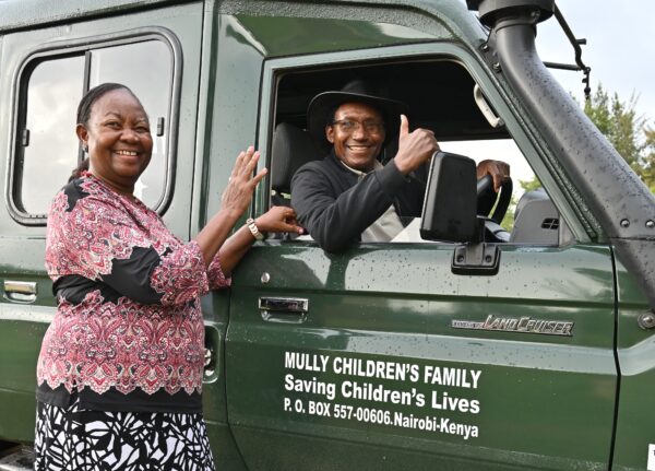 A smiling woman beside an MCF Land Cruiser while the driver gives a thumbs-up