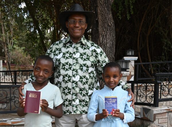 A man in a cowboy hat with two children holding a Bible and a booklet