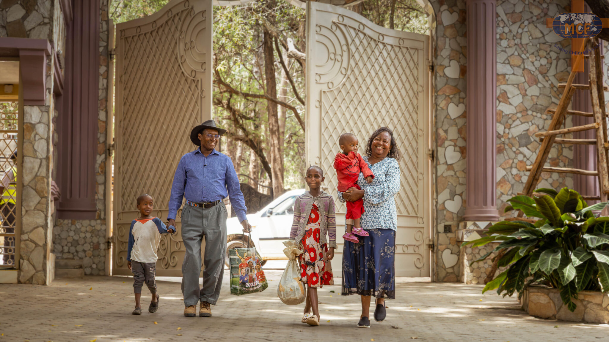 A man in a cowboy hat and a woman carrying a toddler walk with two children through the gates of Mully Children's Family